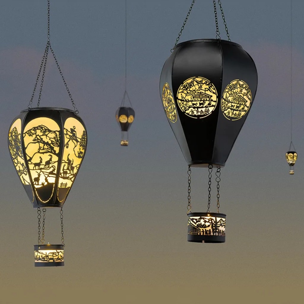 Decorative hanging lanterns with intricate cutouts glowing warm yellow light against a dusk sky.